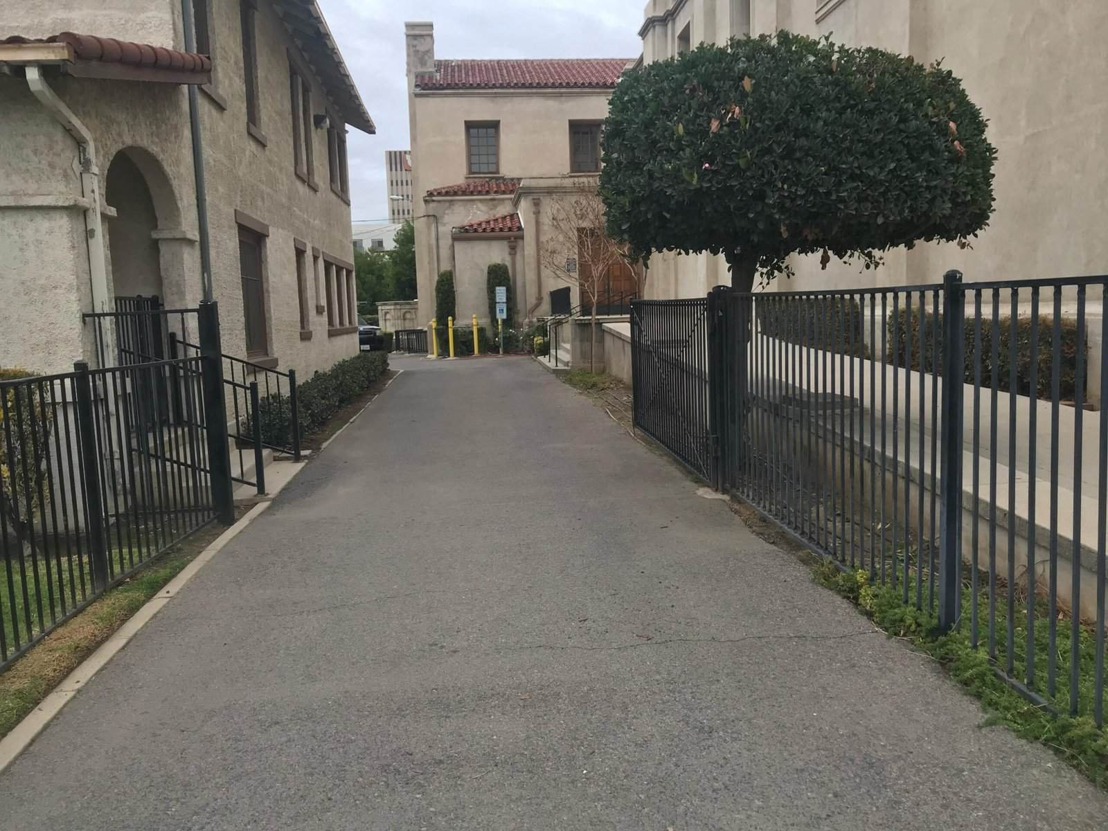 A well-maintained alleyway featuring decorative fencing, trimmed trees, and clean pavement, showcasing professional landscaping services.