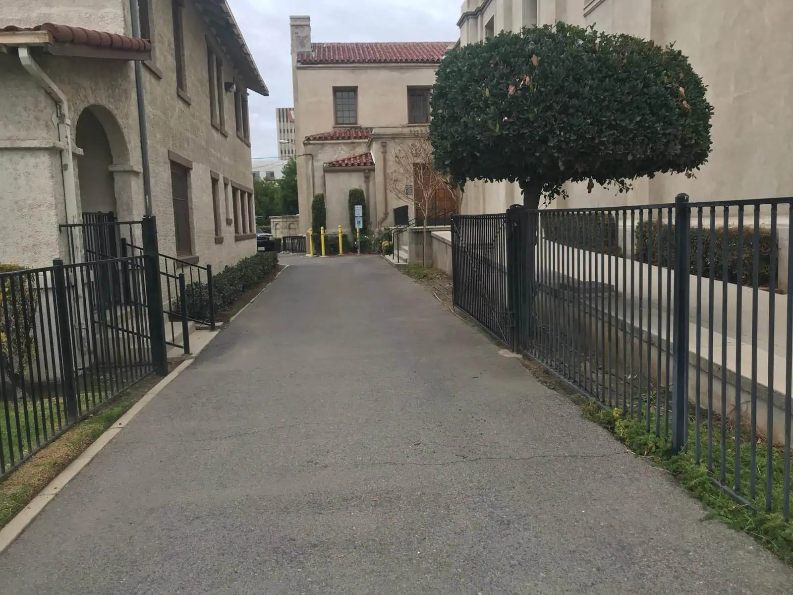 A well-maintained alleyway featuring decorative fencing, trimmed trees, and clean pavement, showcasing professional landscaping services.
